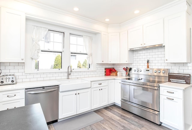 kitchen featuring ornamental molding, a sink, white cabinets, appliances with stainless steel finishes, and light wood-type flooring