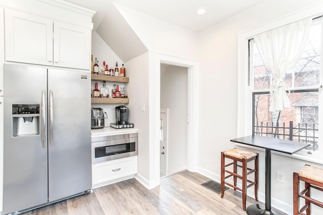 kitchen featuring visible vents, baseboards, light wood-style flooring, stainless steel refrigerator with ice dispenser, and white cabinetry