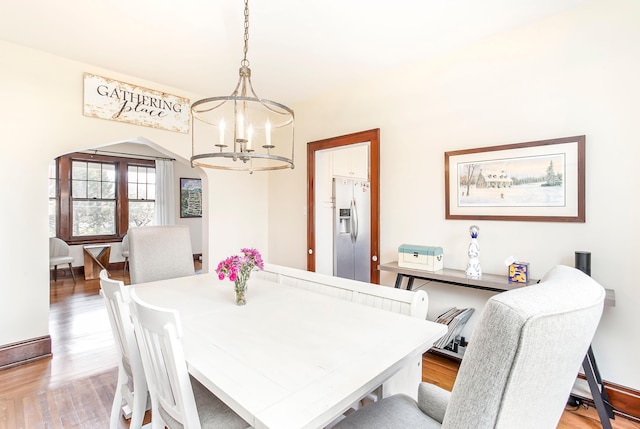 dining area featuring baseboards, arched walkways, light wood-style floors, and an inviting chandelier