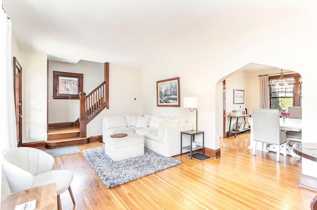 living area featuring stairway, light wood-style flooring, baseboards, and arched walkways