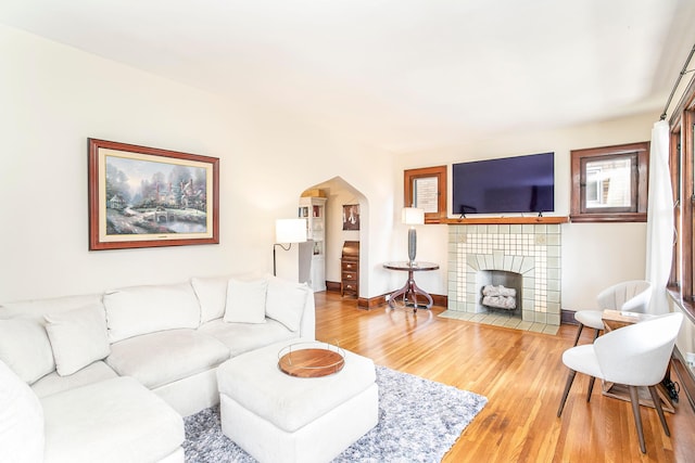 living room with light wood-type flooring, arched walkways, baseboards, and a tiled fireplace