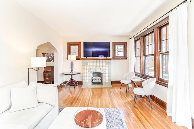 living area featuring arched walkways, baseboards, light wood-type flooring, and a tile fireplace