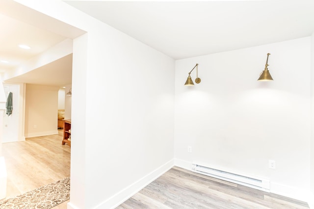 empty room with a baseboard heating unit, baseboards, and light wood finished floors