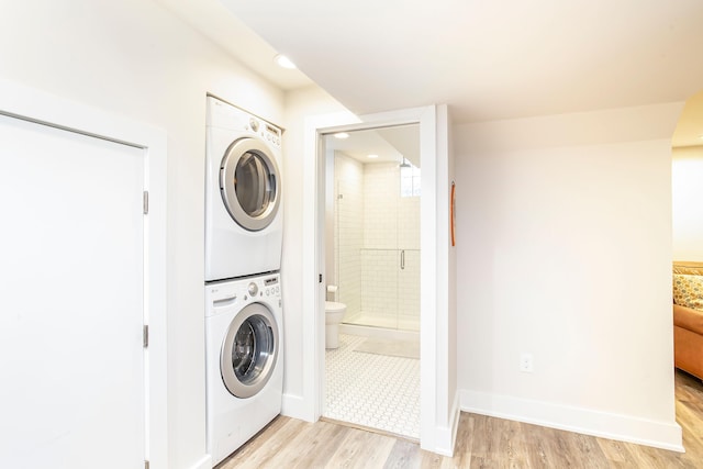 laundry room with light wood finished floors, laundry area, stacked washer and clothes dryer, and baseboards