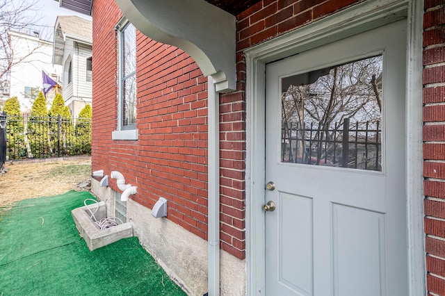 doorway to property featuring brick siding and fence