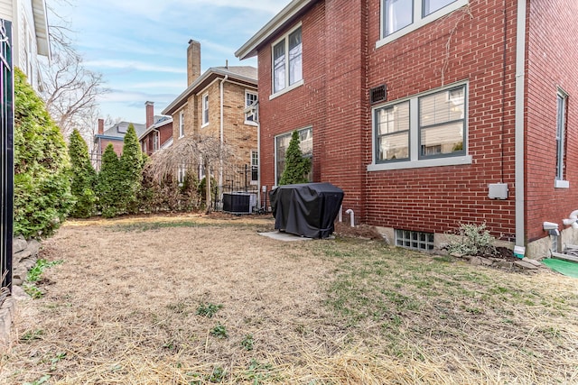 rear view of property featuring a yard, brick siding, and central AC