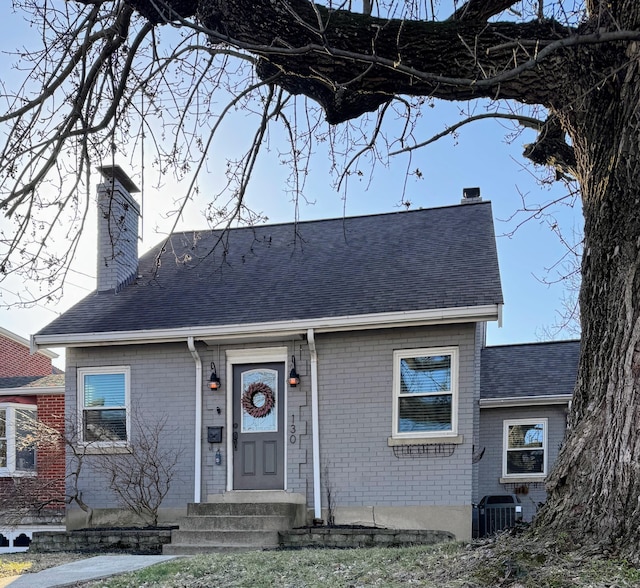 view of front of property featuring central AC unit, brick siding, and a chimney