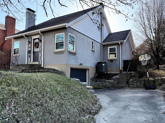 view of front facade with driveway, central AC, an attached garage, brick siding, and a chimney