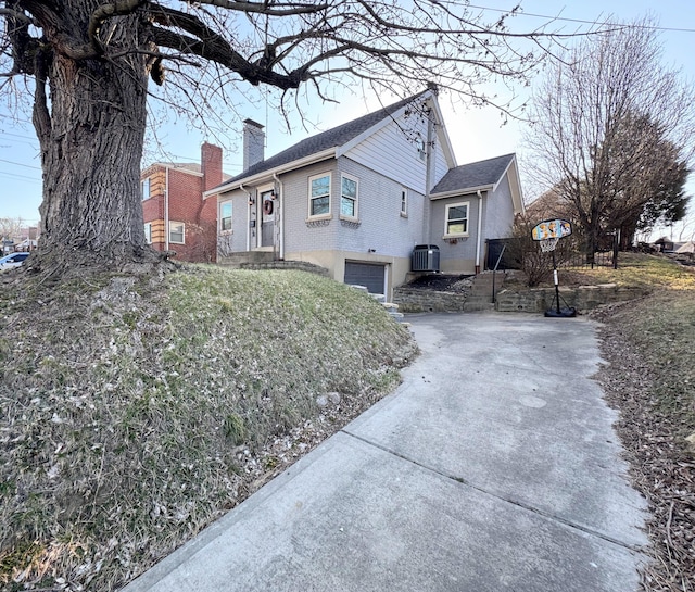 view of side of property with brick siding, concrete driveway, central AC, a chimney, and a garage