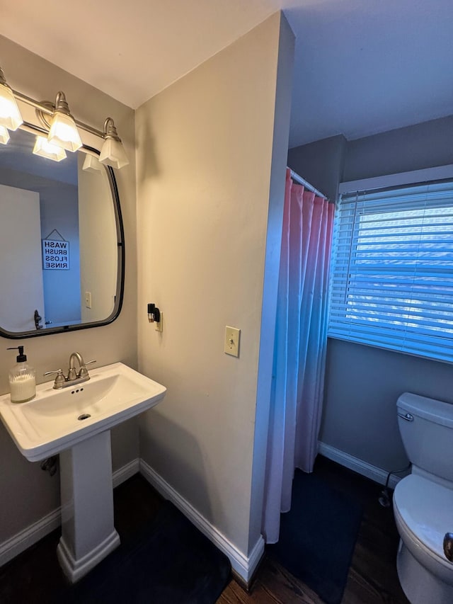 bathroom featuring a shower with shower curtain, toilet, baseboards, and a sink