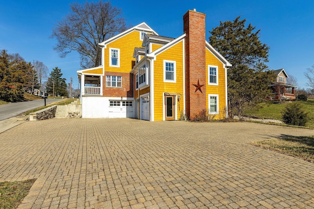 view of front facade with an attached garage, a chimney, and decorative driveway