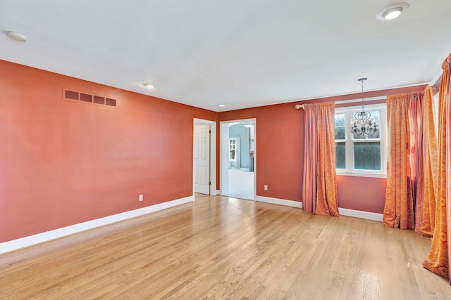 spare room with baseboards, light wood-style floors, visible vents, and a chandelier