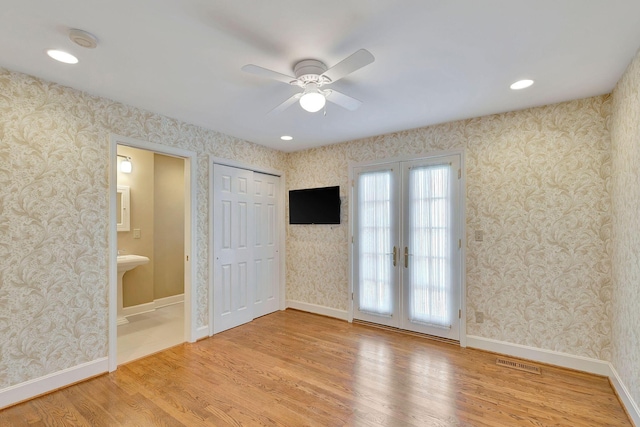 empty room featuring visible vents, wallpapered walls, baseboards, french doors, and wood finished floors