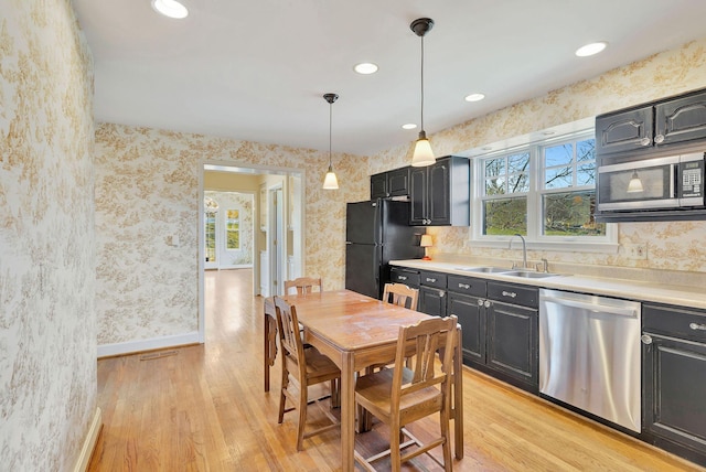 kitchen featuring a sink, stainless steel appliances, light wood-style flooring, and wallpapered walls