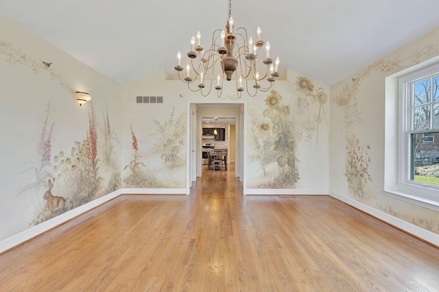 spare room featuring wood finished floors, visible vents, baseboards, vaulted ceiling, and a chandelier