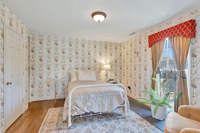 bedroom with visible vents, baseboards, wood finished floors, and wallpapered walls