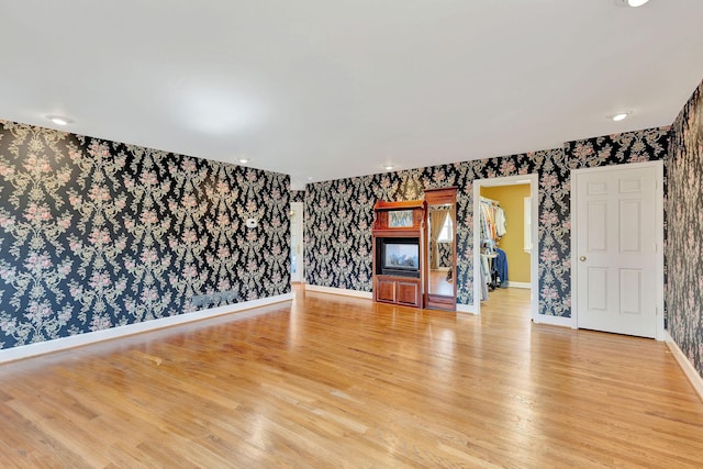 unfurnished living room featuring baseboards, light wood-style flooring, and wallpapered walls