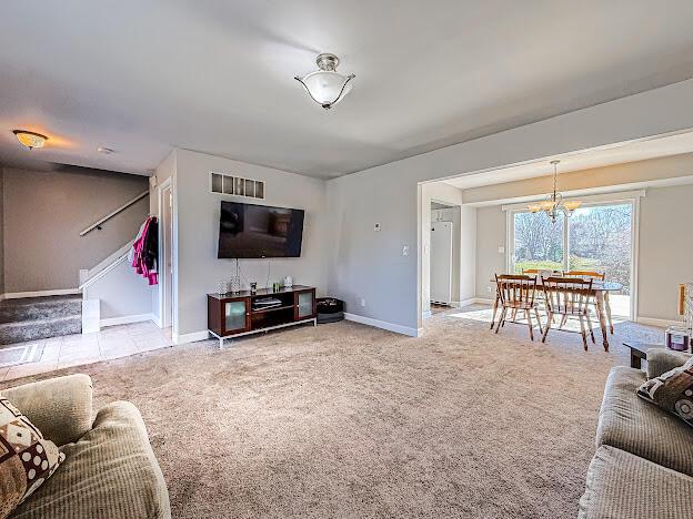 living room featuring a notable chandelier, stairs, baseboards, and carpet floors