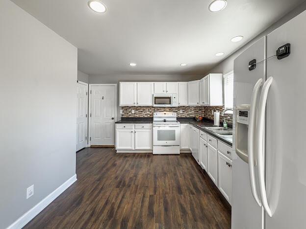 kitchen featuring dark countertops, decorative backsplash, white cabinets, white appliances, and dark wood-style flooring