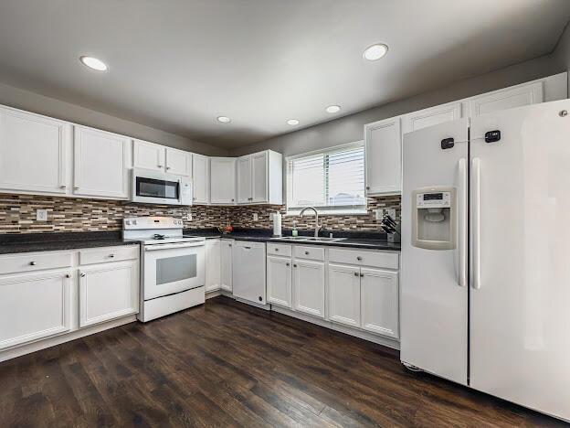 kitchen featuring dark countertops, white appliances, dark wood-type flooring, and a sink