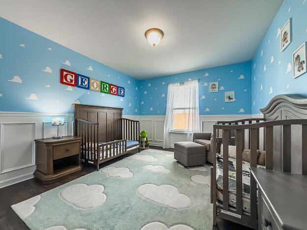 bedroom with a nursery area, wood finished floors, and wainscoting