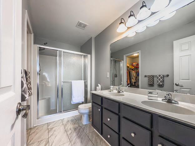 full bathroom with double vanity, a stall shower, toilet, and a sink