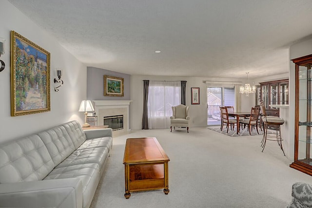 living room with carpet floors, a notable chandelier, a glass covered fireplace, and a textured ceiling