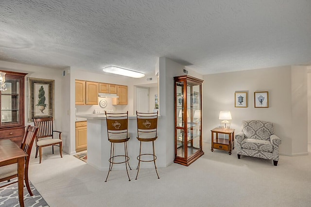 kitchen with a kitchen breakfast bar, light colored carpet, under cabinet range hood, and light brown cabinetry