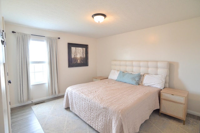 bedroom featuring visible vents, baseboards, light wood-style floors, and a textured ceiling