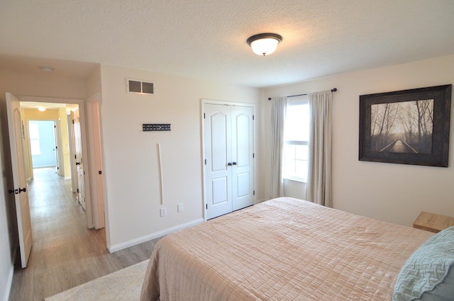 bedroom featuring visible vents, baseboards, light wood-style floors, a closet, and a textured ceiling