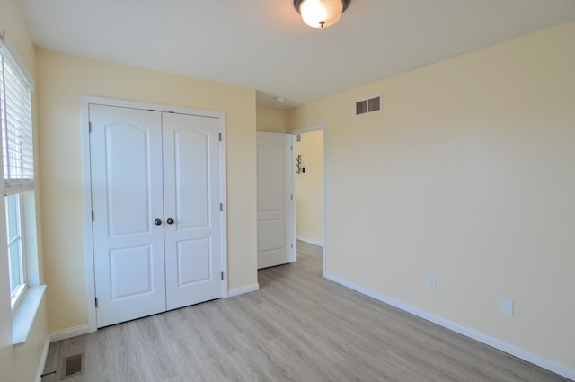 unfurnished bedroom featuring light wood-type flooring, visible vents, baseboards, and a closet