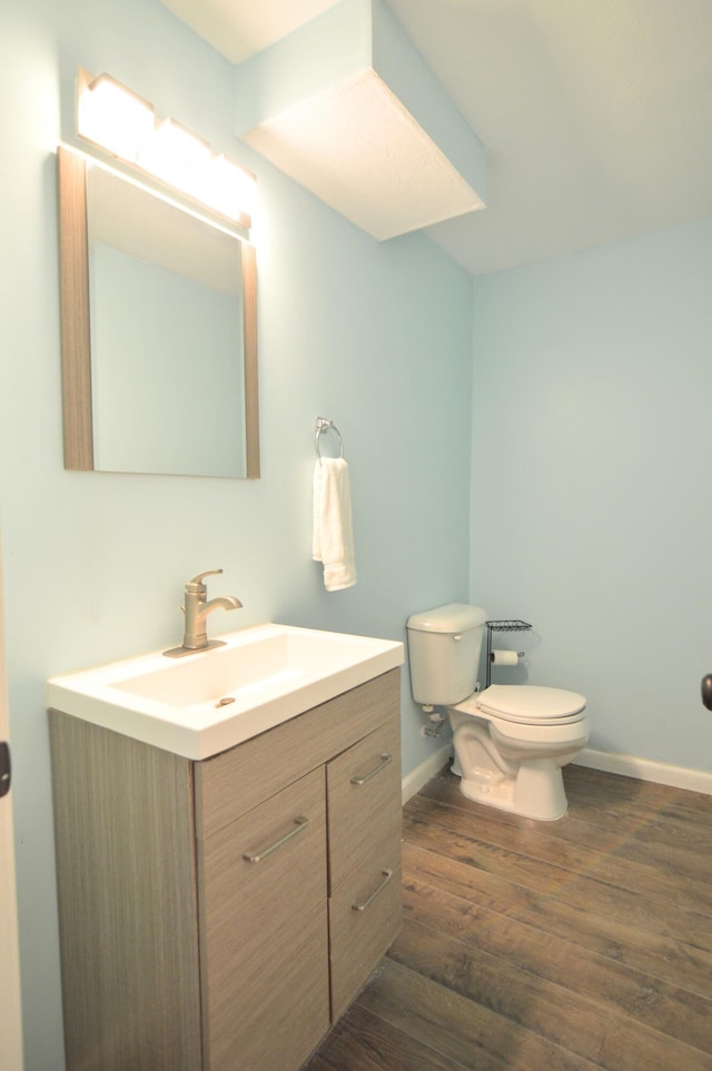 half bathroom featuring toilet, vanity, baseboards, and wood finished floors