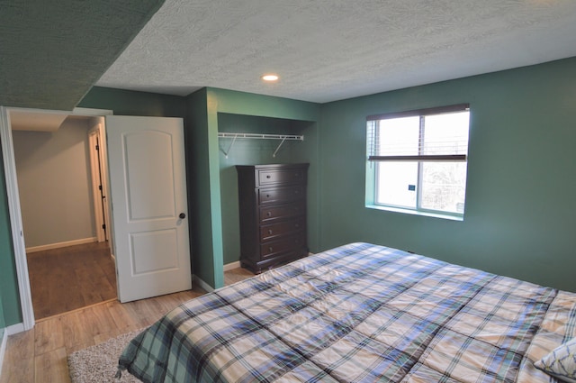 bedroom featuring a textured ceiling, light wood-style floors, a closet, and baseboards