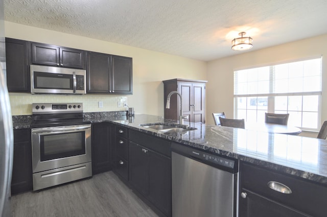 kitchen with dark wood-type flooring, a sink, dark stone countertops, a textured ceiling, and stainless steel appliances