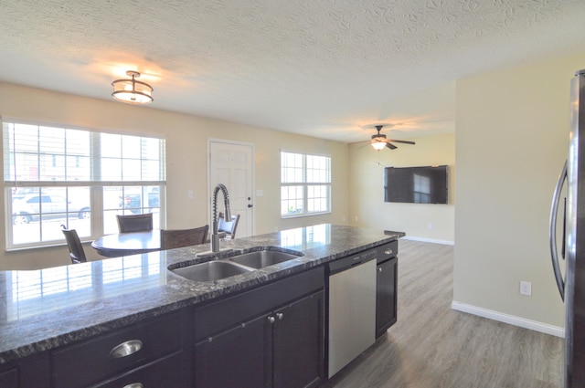 kitchen with dark stone counters, stainless steel appliances, a sink, light wood-style floors, and open floor plan