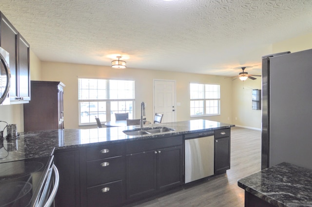 kitchen with dark stone counters, a sink, stainless steel appliances, dark wood-type flooring, and open floor plan