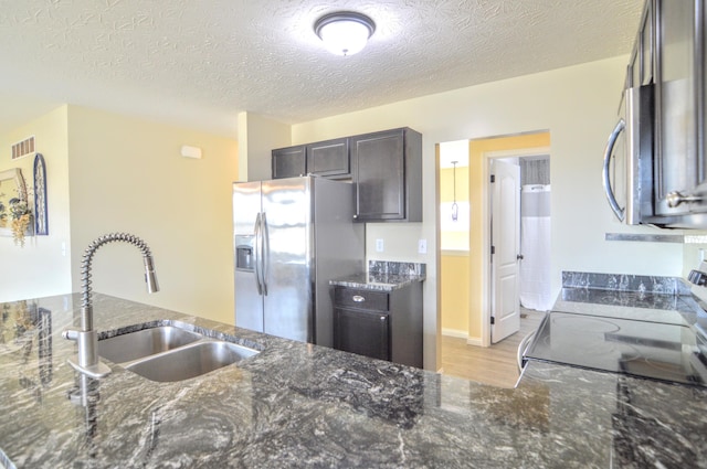 kitchen with visible vents, stainless steel fridge with ice dispenser, dark brown cabinetry, dark stone counters, and a sink