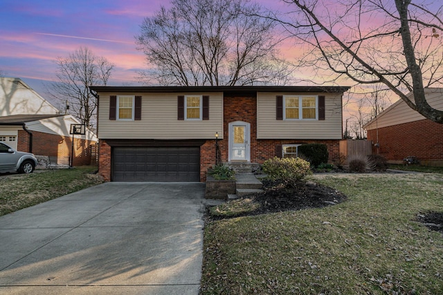 raised ranch with driveway, brick siding, an attached garage, and a front lawn