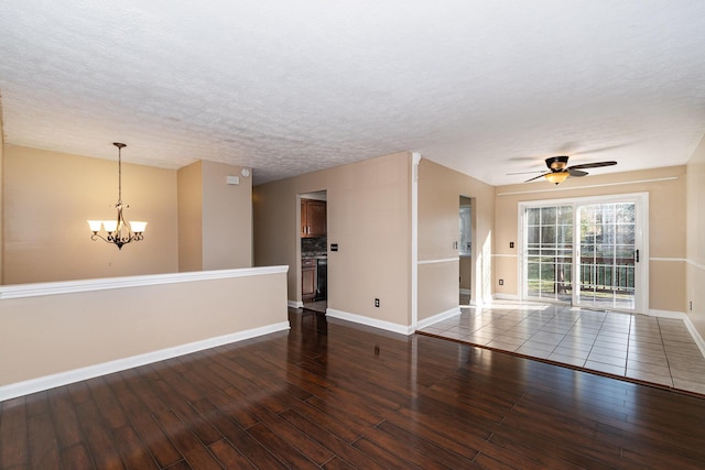 empty room with ceiling fan with notable chandelier, wood finished floors, baseboards, and a textured ceiling