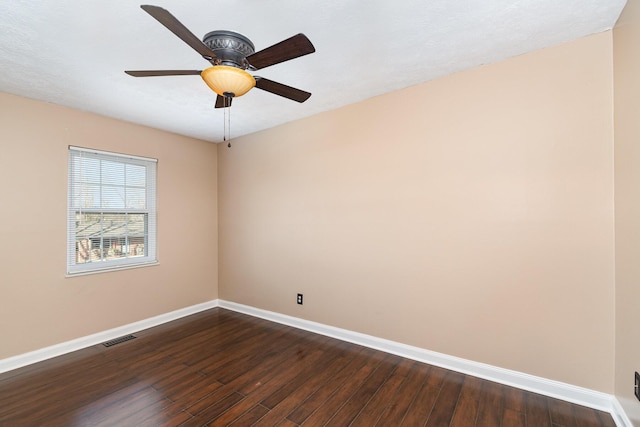 spare room with a ceiling fan, dark wood-style floors, visible vents, and baseboards