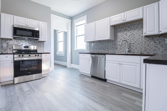 kitchen featuring dark countertops, white cabinets, appliances with stainless steel finishes, and light wood-style flooring