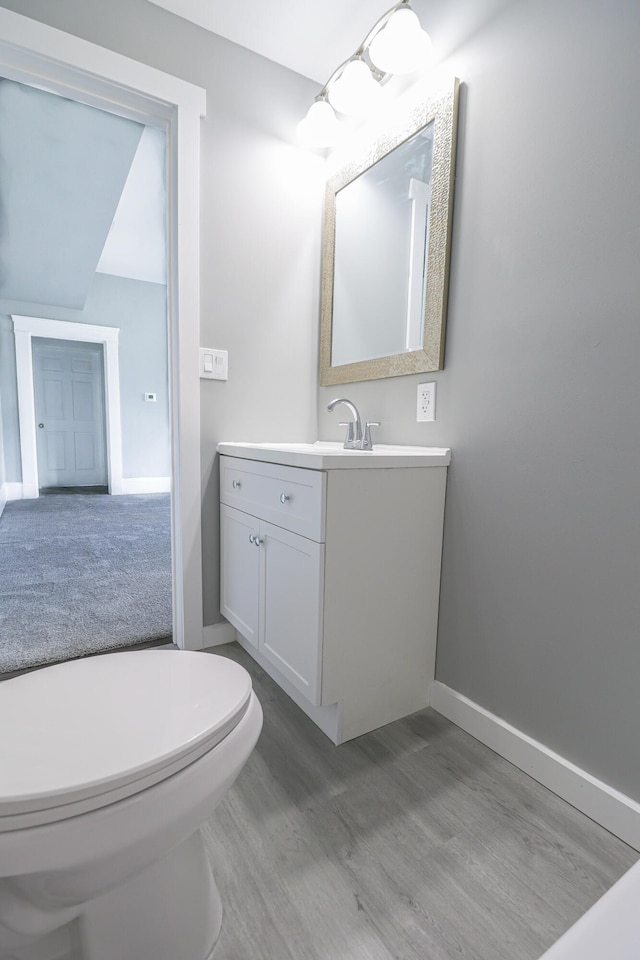 bathroom with toilet, vanity, baseboards, and wood finished floors