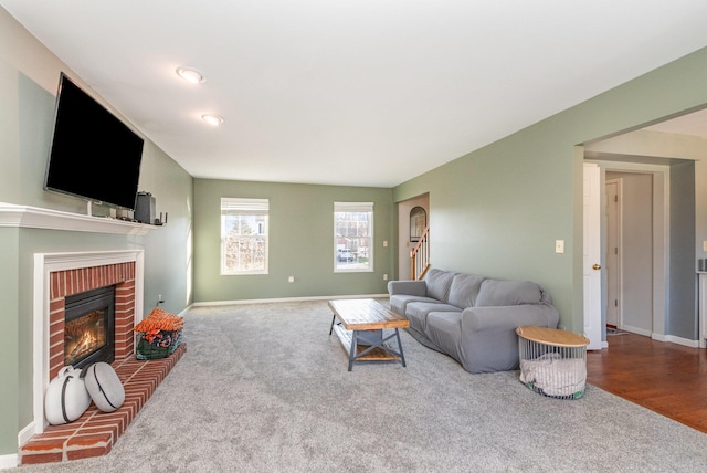 carpeted living area featuring stairway, a fireplace, and baseboards