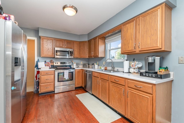 kitchen with dark wood-type flooring, light countertops, brown cabinetry, stainless steel appliances, and a sink