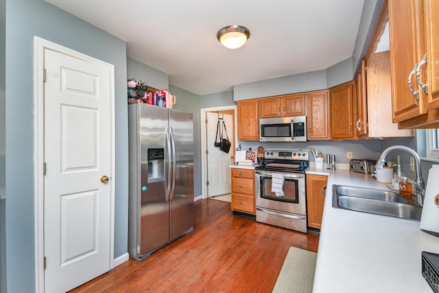 kitchen featuring a sink, light countertops, dark wood-type flooring, appliances with stainless steel finishes, and brown cabinets