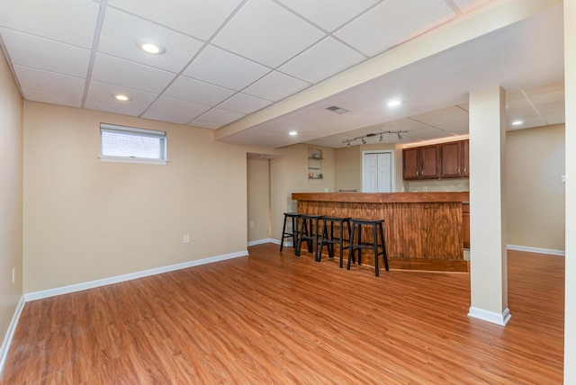 interior space with baseboards, a breakfast bar area, a paneled ceiling, and light wood-style floors