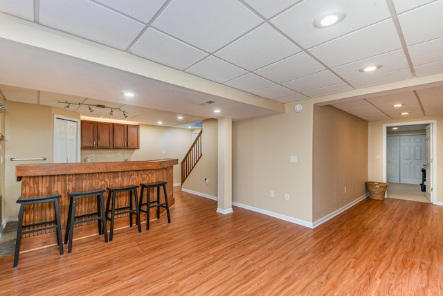 kitchen featuring baseboards, light wood finished floors, rail lighting, a kitchen breakfast bar, and brown cabinets