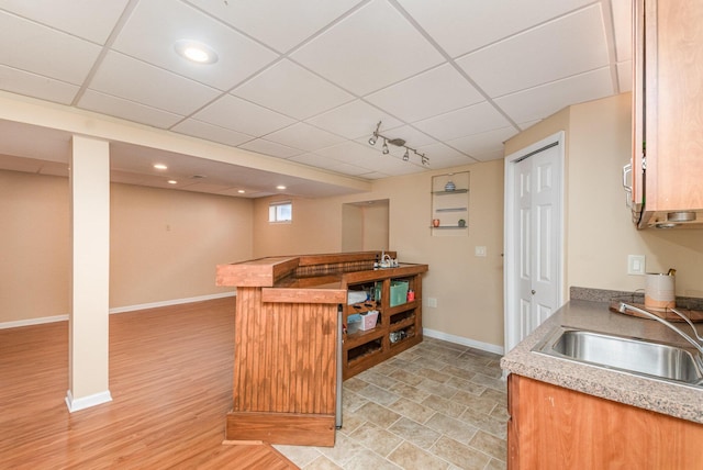 kitchen featuring a drop ceiling, light countertops, baseboards, and a sink