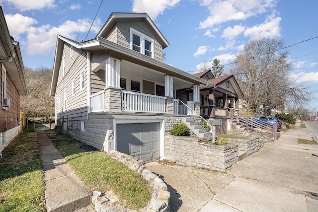 bungalow-style house with stairway, covered porch, an attached garage, and driveway