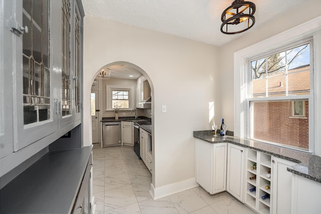 kitchen with marble finish floor, a sink, dark stone countertops, stainless steel dishwasher, and baseboards